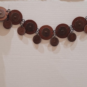 Puede incluir: Un cinturón de metal marrón con una cadena y múltiples abalorios redondos con forma de monedas.