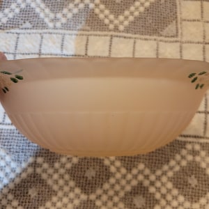 Könnte beinhalten: Eine blassrosa gefrostete Glasschüssel mit einem gewellten Rand und grünen Blumendesigns. Die Schüssel ist leer und steht auf einer weißen und grauen gemusterten Oberfläche.