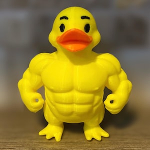 Puede incluir: Un pato de goma amarillo con un cuerpo musculoso. El pato tiene un pico naranja brillante y ojos negros.