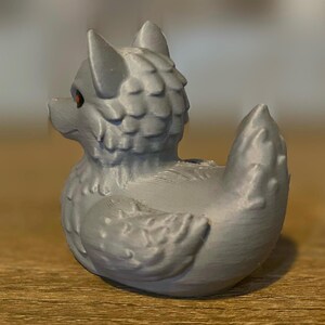 A gray 3D printed duckies shaped like wolves with red eyes. The duckies are sitting on a wooden surface. Rubber Duck style. Facing left