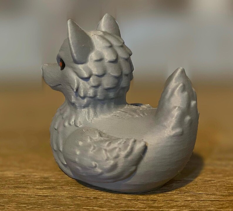 A gray 3D printed duckies shaped like wolves with red eyes. The duckies are sitting on a wooden surface. Rubber Duck style. Facing left