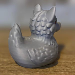 A gray 3D printed duckies shaped like wolves with red eyes. The duckies are sitting on a wooden surface. Rubber Duck style. Facing back right.