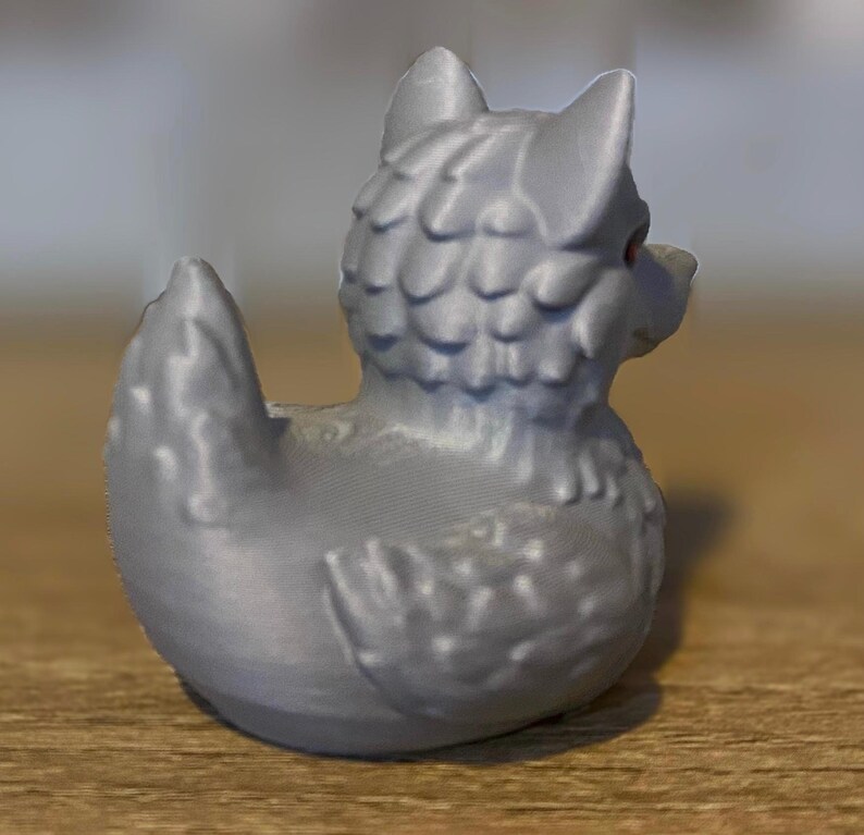 A gray 3D printed duckies shaped like wolves with red eyes. The duckies are sitting on a wooden surface. Rubber Duck style. Facing back right.