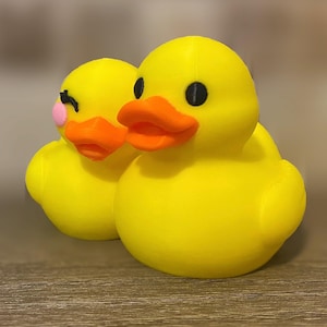 3D printed couples Duck of a girlfriend and a boyfriend all yellows ducks connected with orange beaks and black eyes. Girlfriend duck has eyelashes and pink Rosie cheek. Rubber Duck style perfect for jeep ducking. Facing left front.