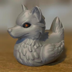 A gray 3D printed duckies shaped like wolves with red eyes. The duckies are sitting on a wooden surface. Rubber Duck style.