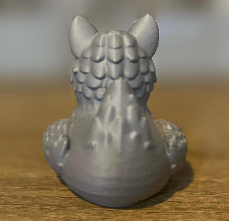 A gray 3D printed duckies shaped like wolves with red eyes. The duckies are sitting on a wooden surface. Rubber Duck style. Facing backwards.