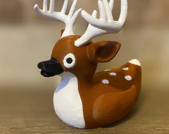 Puede incluir: Una figura con forma de ciervo marrón y blanco con cuernos blancos, pico negro y manchas blancas en la espalda. El ciervo tiene ojos grandes y redondos y probablemente sea un objeto decorativo o un juguete.
