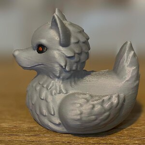 A gray 3D printed duckies shaped like wolves with red eyes. The duckies are sitting on a wooden surface. Rubber Duck style. Facing left