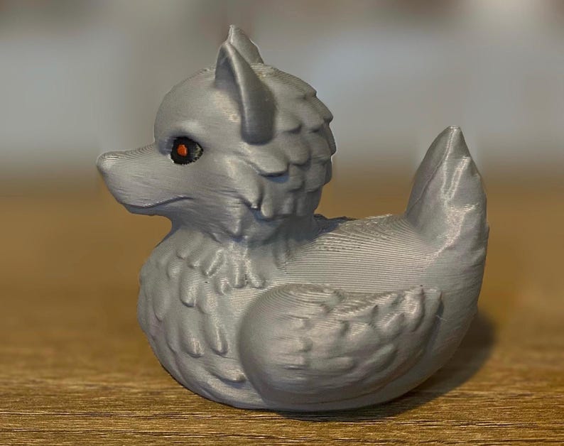 A gray 3D printed duckies shaped like wolves with red eyes. The duckies are sitting on a wooden surface. Rubber Duck style. Facing left