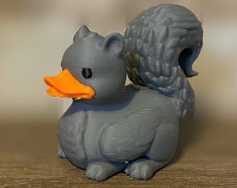 Puede incluir: Un pato gris impreso en 3D con un pico naranja y una cola gris tupida.