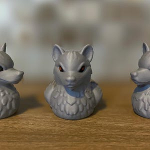 Three gray 3D printed duckies shaped like wolves with red eyes. The duckies are sitting on a wooden surface. Rubber Duck style.
