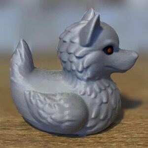 A gray 3D printed duckies shaped like wolves with red eyes. The duckies are sitting on a wooden surface. Rubber Duck style. Facing right.