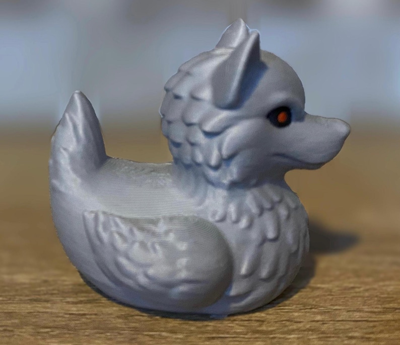 A gray 3D printed duckies shaped like wolves with red eyes. The duckies are sitting on a wooden surface. Rubber Duck style. Facing right.