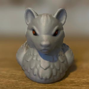 A gray 3D printed duckies shaped like wolves with red eyes. The duckies are sitting on a wooden surface. Rubber Duck style. Facing foward