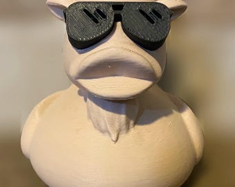 Puede incluir: Un pato de goma blanco con cuernos y gafas de sol negras. El pato tiene una superficie texturizada y una cara detallada.