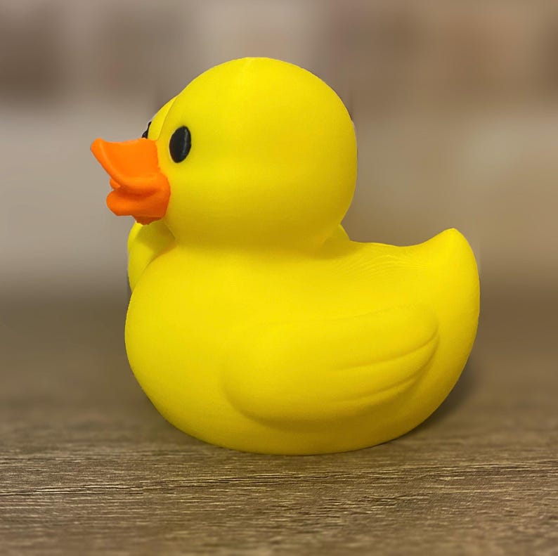 3D printed couples Duck of a girlfriend and a boyfriend all yellows ducks connected with orange beaks and black eyes. Girlfriend duck has eyelashes and pink Rosie cheek. Rubber Duck style perfect for jeep ducking. Facing left.