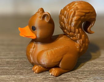 Puede incluir: Una figurita de ardilla de impresión 3D marrón con un pico de pato. La ardilla tiene una cola tupida y está sentada sobre una superficie de madera.