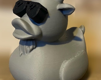 Puede incluir: Un pato de goma gris con cuernos y gafas de sol negras. El pato está hecho de un material impreso en 3D.
