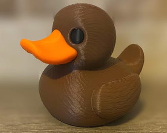 Puede incluir: Figura de pato marrón impresa en 3D con pico naranja y ojos negros. El pato tiene un cuerpo liso y redondeado y una superficie texturizada. Este artículo decorativo es adecuado para la decoración del hogar. Mide unos 10 cm de largo.