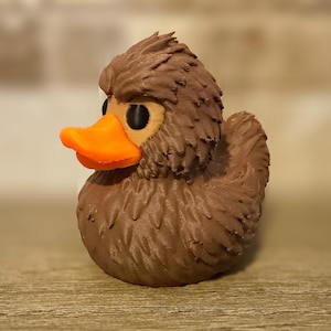 May include: A brown, textured duck figurine with an orange beak and black eyes. The duck has a detailed, feathery appearance, giving it a unique, handcrafted look. This decorative item is suitable for home decor or as a collectible.