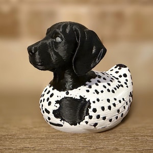May include: A black and white decorative figurine of a dog, resembling a duck. The dog's head is black, with a detailed texture. The body is white with black spots, creating a Dalmatian-like pattern. The figurine is set against a blurred background.
