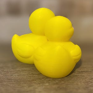 3D printed couples Duck of a girlfriend and a boyfriend all yellows ducks connected with orange beaks and black eyes. Girlfriend duck has eyelashes and pink Rosie cheek. Rubber Duck style perfect for jeep ducking. Facing back right.