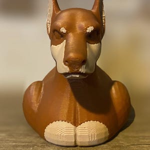 May include: A brown and white Doberman Pinscher bust. The dog sculpture has a textured surface and is in a seated position. The dog's face is white with brown markings, and it has pointed ears.