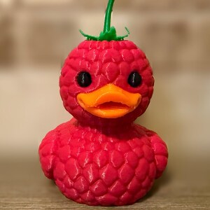 May include: A whimsical, red duck figurine with a raspberry-like texture. It features black eyes, an orange beak, and a green stem on top. The duck is a unique decorative item.