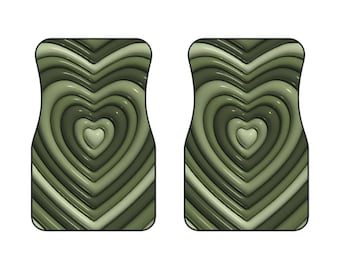May include: Two car floor mats with a heart design. The mats are olive green with a glossy finish. The heart design is made up of concentric layers of hearts in varying shades of green, creating a 3D effect. The mats have a rectangular shape with a curved top.