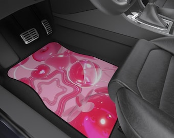 May include: Pink car floor mat featuring a repeating pattern of 3D-rendered pink hearts, stars, and bubble shapes. The mat is positioned in the driver's side footwell of a car, with pedals and seat visible.