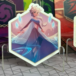 May include: A hexagonal sticker featuring a cartoon illustration of a woman with long blonde hair wearing a blue and white dress. The background is a light blue and purple gradient with white snowflakes.