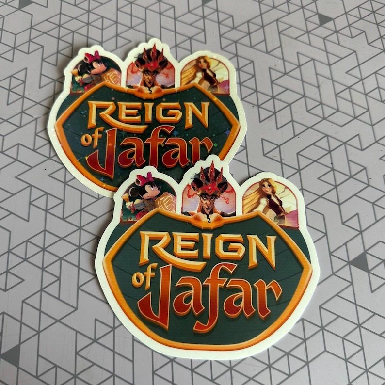 K&ouml;nnte beinhalten: Zwei Aufkleber mit gr&uuml;nem Hintergrund und goldener Schrift, die "Reign of Jafar" lautet. Die Aufkleber zeigen Comicbilder von Jafar, Jasmin und Aladdin.
