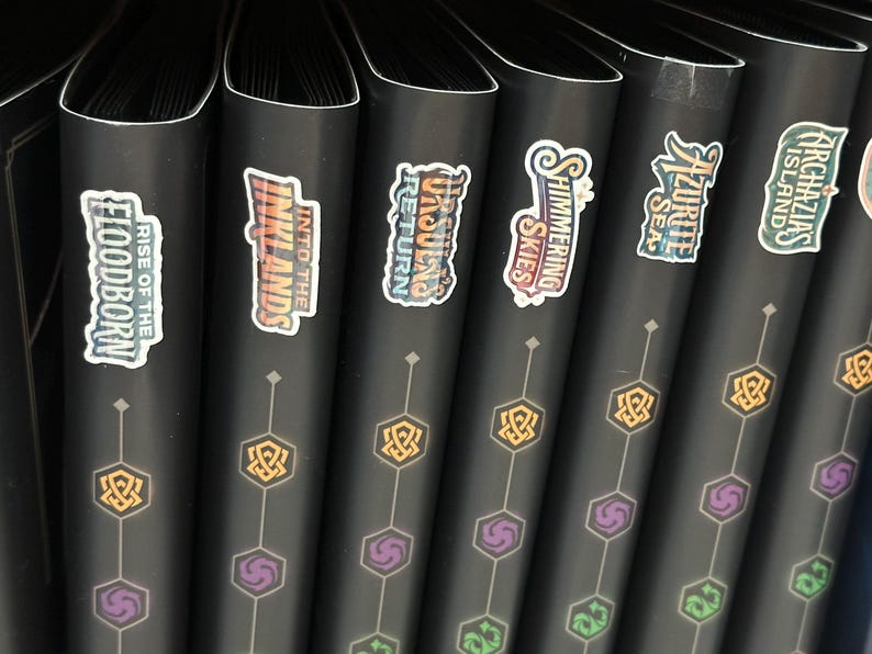 May include: A row of black binders with colorful stickers. The stickers display text such as "Rise of the Floodborn", "Into the Inklands", and "Unbound Return". Each binder has a geometric design in gold and purple.