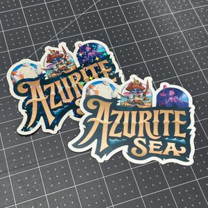 K&ouml;nnte beinhalten: Zwei Aufkleber mit einem blauen und goldenen Design mit dem Text "Azurite Sea". Die Aufkleber zeigen Comicfiguren aus dem Disney-Film Lilo & Stitch.