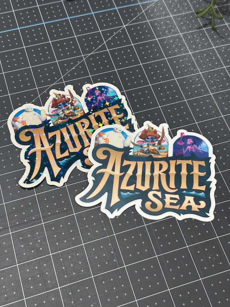 K&ouml;nnte beinhalten: Zwei Aufkleber mit einem blauen und goldenen Design mit dem Text "Azurite Sea". Die Aufkleber zeigen Comicfiguren aus dem Disney-Film Lilo & Stitch.