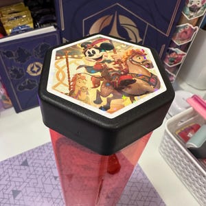 May include: A hexagonal container with a translucent red body and a black lid. The top of the lid features a holographic sticker depicting Mickey Mouse riding a carousel horse, surrounded by small star-shaped sparkles and colorful carousel elements.