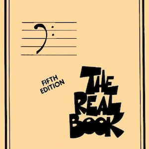 May include: A tan book cover with a black decorative border. The cover features a bass clef and staff, the words "FIFTH EDITION", and the title "THE REAL BOOK" in bold, black lettering. The design is simple and classic.