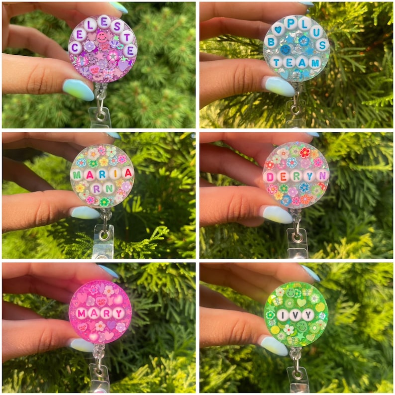 May include: A collection of six circular badge reels featuring clear resin filled with colorful confetti, including flowers, hearts, and smiley faces. Each reel displays a name or phrase spelled out with white letter beads: CELESTE, B PLUS TEAM, MARIA RN, DERYN, MARY, and IVY.