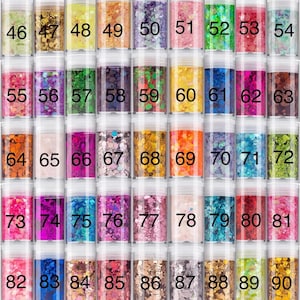 May include: A collection of forty-five clear cylindrical jars filled with various colors of decorative craft glitter. Each jar is labeled with a black number ranging from 46 to 90, showcasing a wide spectrum of hues including gold, pink, blue, green, and purple.