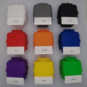 May include: Nine small square boxes in various colors, including white, grey, black, red, orange, blue, purple, yellow, and green. Each box has a label with the color name printed on it.