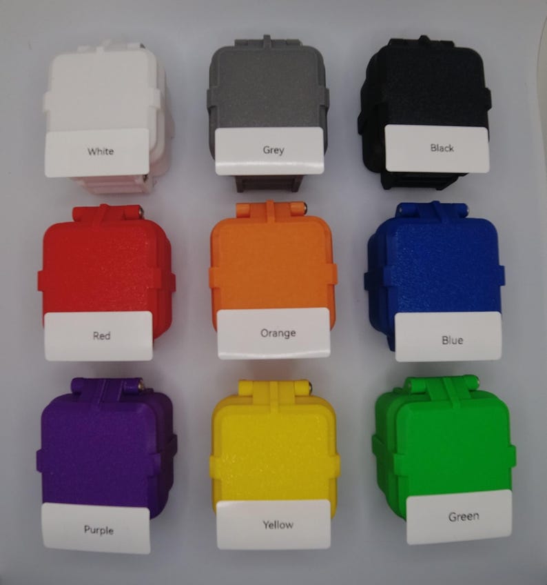 May include: Nine small square boxes in various colors, including white, grey, black, red, orange, blue, purple, yellow, and green. Each box has a label with the color name printed on it.