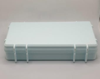 Könnte beinhalten: Ein rechteckiger Aufbewahrungsbehälter aus hellblauem Kunststoff mit einer strukturierten Oberfläche auf der Oberseite und einem glatten, verstärkten Rand. Das Gehäuse hat vier vertikale, riegelartige Vorsprünge an der Vorderseite.