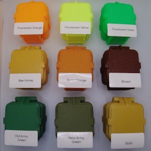 May include: Nine small square containers with different colored paint samples. The colors are fluorescent orange, fluorescent yellow, fluorescent green, bee honey, burnt orange, brown, old army green, new army green, and gold.