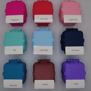 May include: Nine small square containers with different colors, including magenta, hot pink, light pink, teal, light blue, dark blue, peacock, merlot, and violet. Each container has a label with the color name.