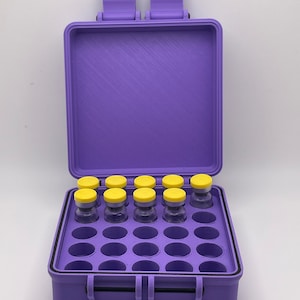 May include: A purple plastic case with a black rubber seal and a handle. The case has 24 compartments, each with a small vial with a yellow lid. The case is open and the vials are visible.