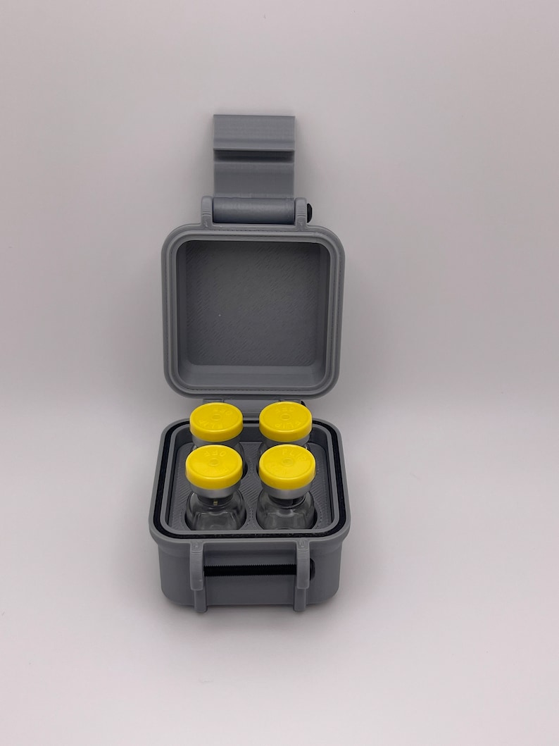 May include: A gray plastic case with a hinged lid, containing four small glass vials with yellow caps. The case has a carrying handle.