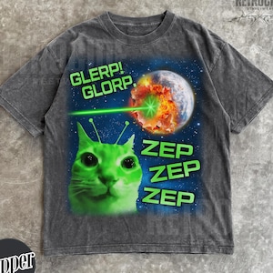 May include: Dark gray t-shirt featuring a green alien cat with antennae, a planet being destroyed by a green laser, and the text "GLERP! GLORP." and "ZEP ZEP ZEP." The shirt has a vintage, distressed look.