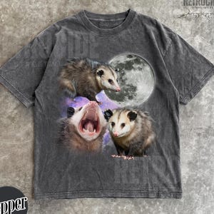 May include: Dark gray t-shirt featuring a graphic of three opossums with a full moon and a galaxy background. The opossums are in various poses, with one yawning. The shirt has a vintage, distressed look.