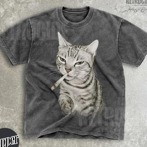 May include: Dark gray t-shirt featuring a detailed illustration of a gray tabby cat with a cigarette in its mouth. The shirt has the text "RETROCIDE STREETWEAR" and "Pepper" on it.