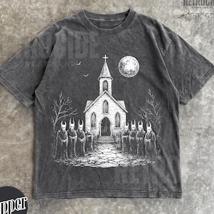 May include: A charcoal gray short-sleeve t-shirt featuring a white graphic print of a church with a steeple, a full moon, and a group of hooded figures with horned masks standing in front. The shirt has a distressed, washed-out fabric appearance.